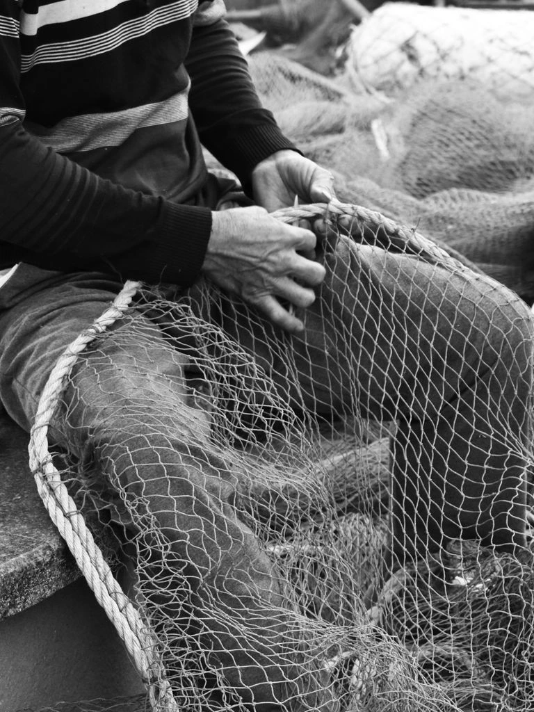 Dawn still of a fisherman mending nets on an Icelandic black sand beach.